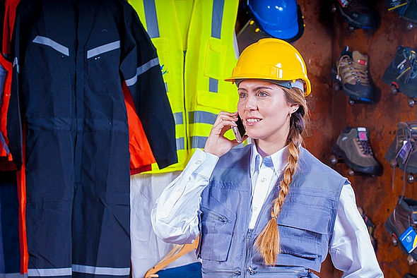 Frau mit Mobiltelefon vor Arbeitsschutzkleidung